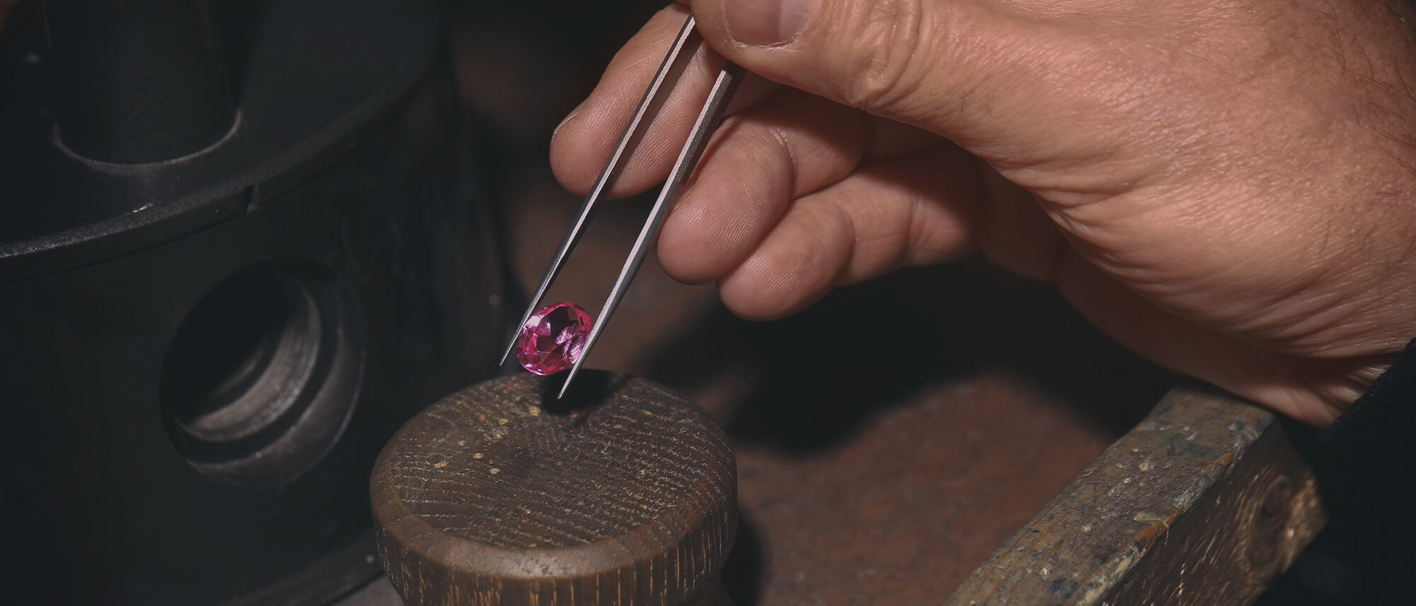 Mens hand holding pink gemstone in tweezers 